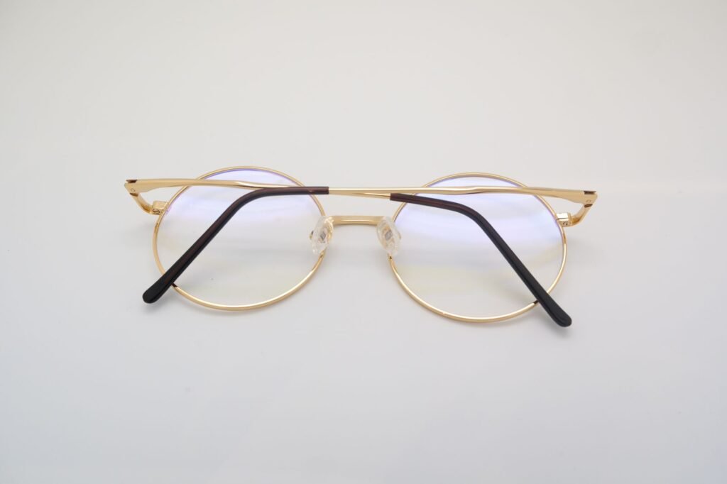 Round gold metal eyeglasses with dark temple tips resting on a light gray surface