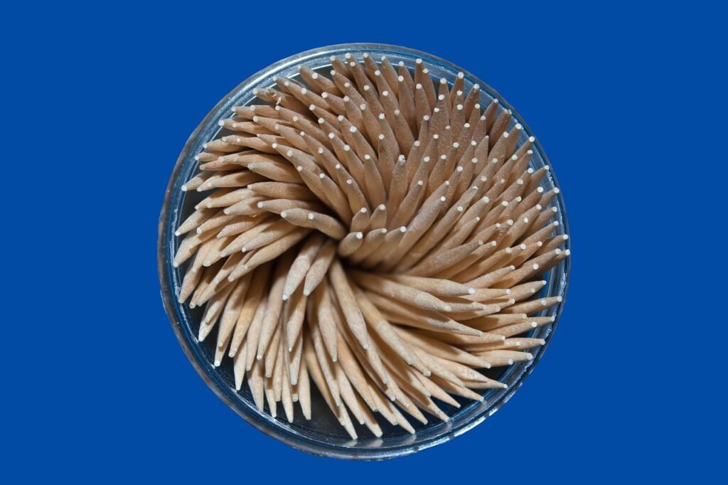 Round glass holder packed with wooden toothpicks seen from above on a blue background