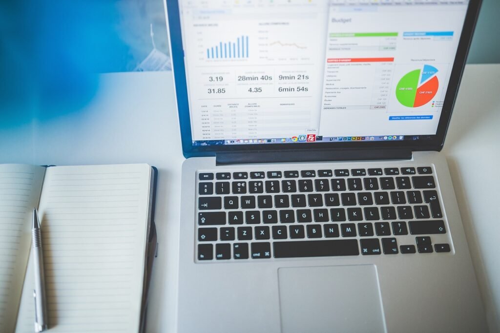Open laptop displaying charts and a pie graph on a white desk beside a notebook and pen