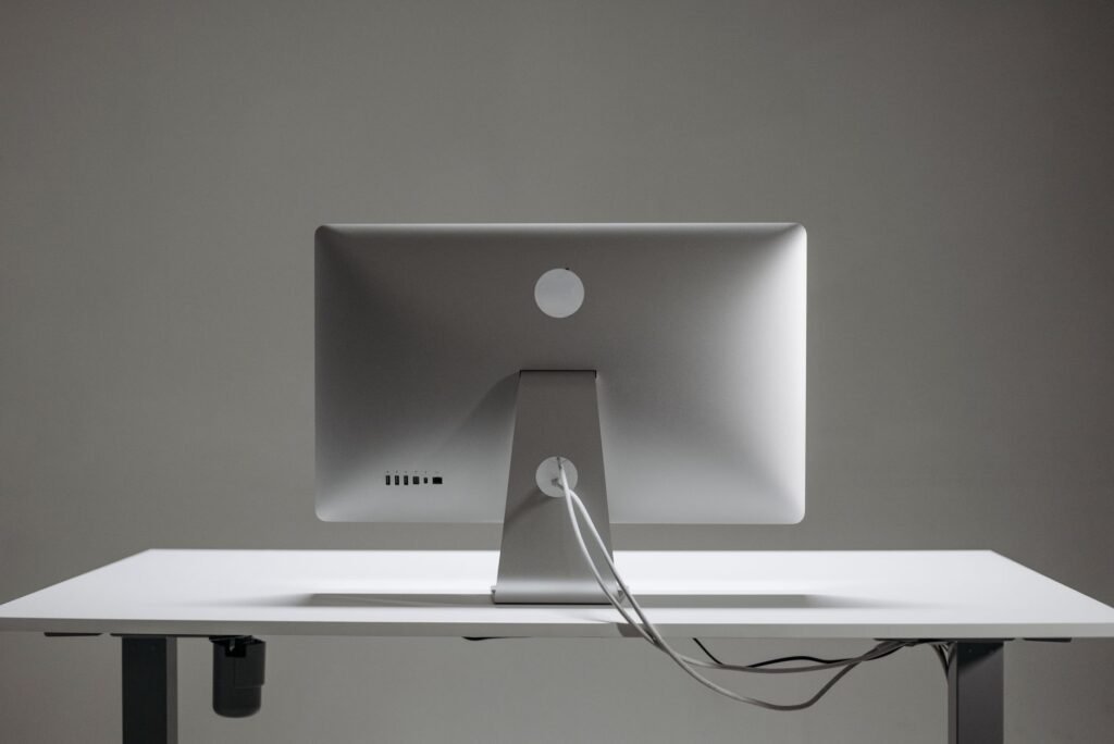 Back of a silver monitor on a white desk with its cable routed through the stand