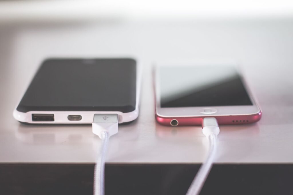 Two smartphones lying on a table with white charging cables plugged into their ports
