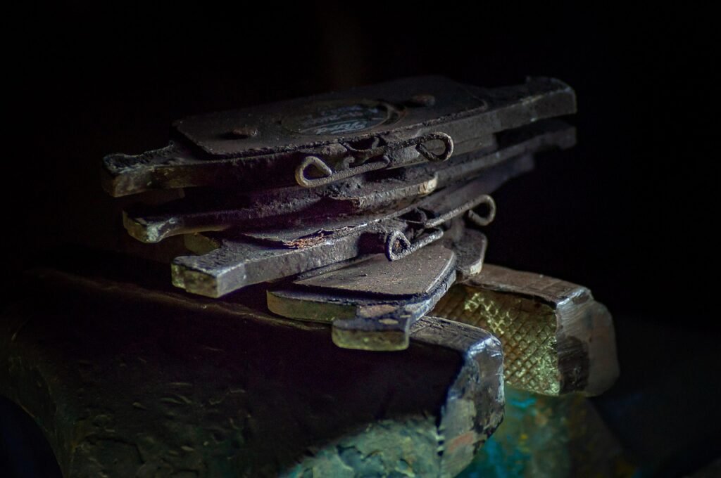Several used brake pads with metal backing plates stacked on a vise against a dark background