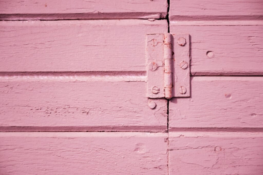 Metal butt hinge joining a pink painted wooden door and its frame