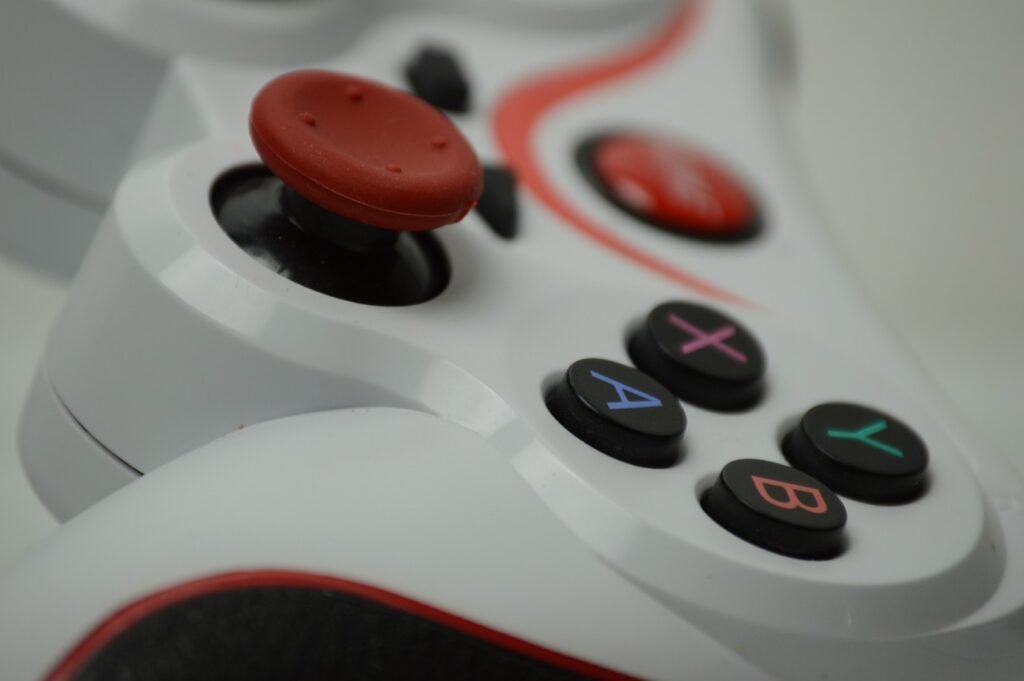 Close view of a white game controller thumbstick with a red cap beside lettered face buttons