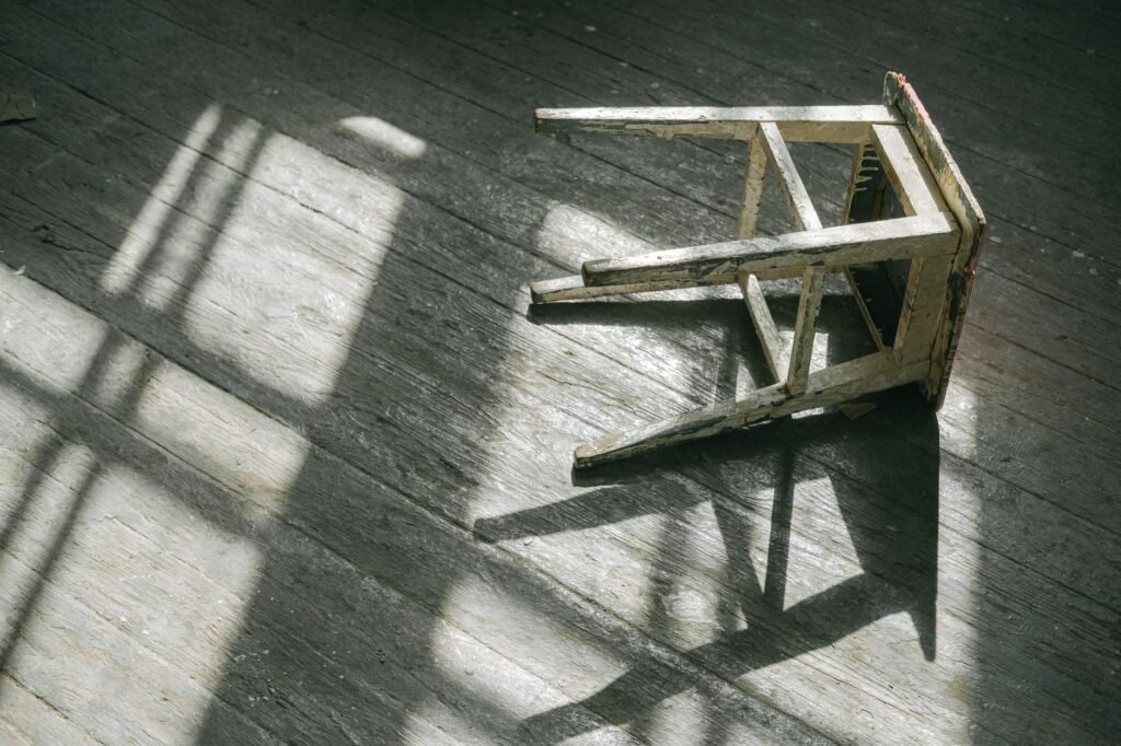 White wooden chair lying upside down on a wooden floor in window light