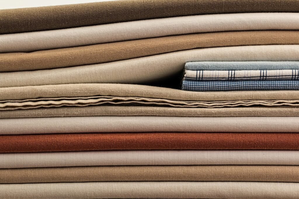 Tall stack of folded linens in beige, brown and rust tones with a checked cloth tucked in