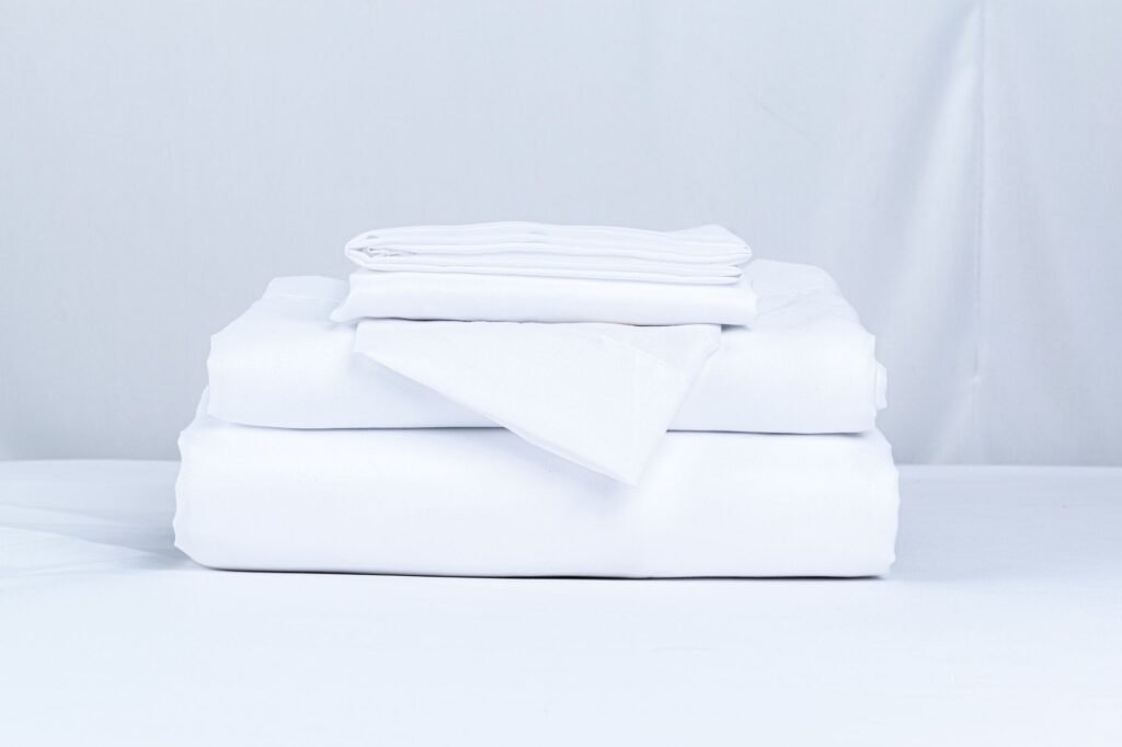 Stack of neatly folded white bed sheets and pillowcases on a white bed