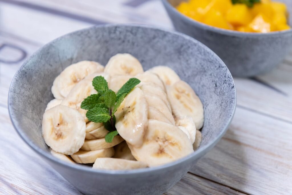Gray bowl of sliced bananas topped with a sprig of mint
