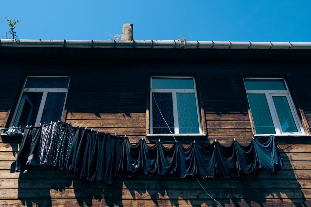 Low angle view of wooden building with laundry drying on clothesline under clear blue sky
