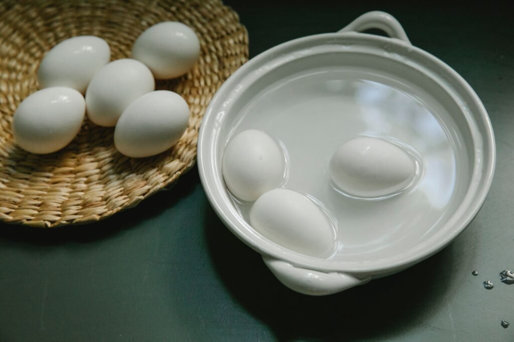 From above of fresh healthy white chicken boiled eggs in saucepan and wicker plate placed on table in kitchen