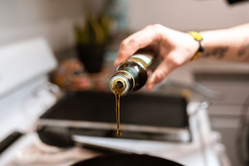 A focused image showing olive oil being poured from a bottle into a pan during cooking