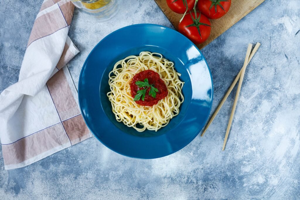 Top view of spaghetti with tomato sauce garnished with parsley, served on a blue plate