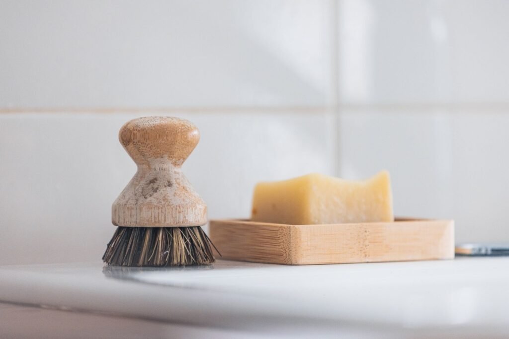 A wooden cleaning brush beside a bar of soap in a minimal indoor setting