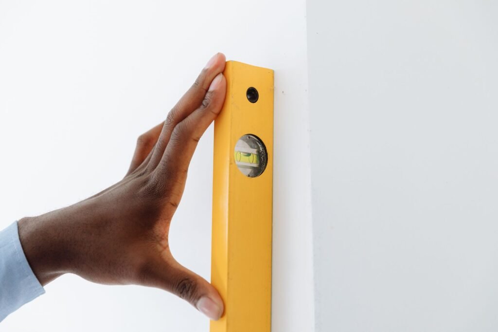 Hand pressing a yellow spirit level flat against a white wall