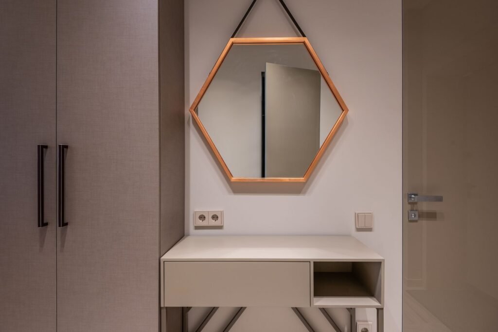 Tall beige cabinet doors with long black bar pulls next to a vanity and hexagon mirror