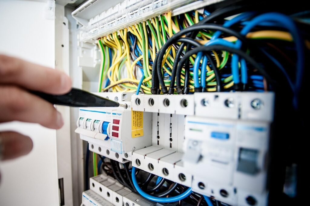 Hand holding a voltage tester screwdriver against wiring in an open electrical panel with breakers