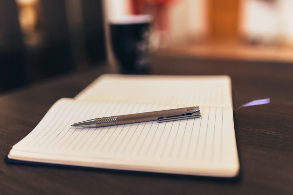 Open lined notebook with a silver pen resting on a dark wooden desk