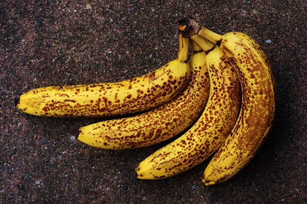Bunch of very ripe bananas covered in brown speckles lying on a dark stone surface