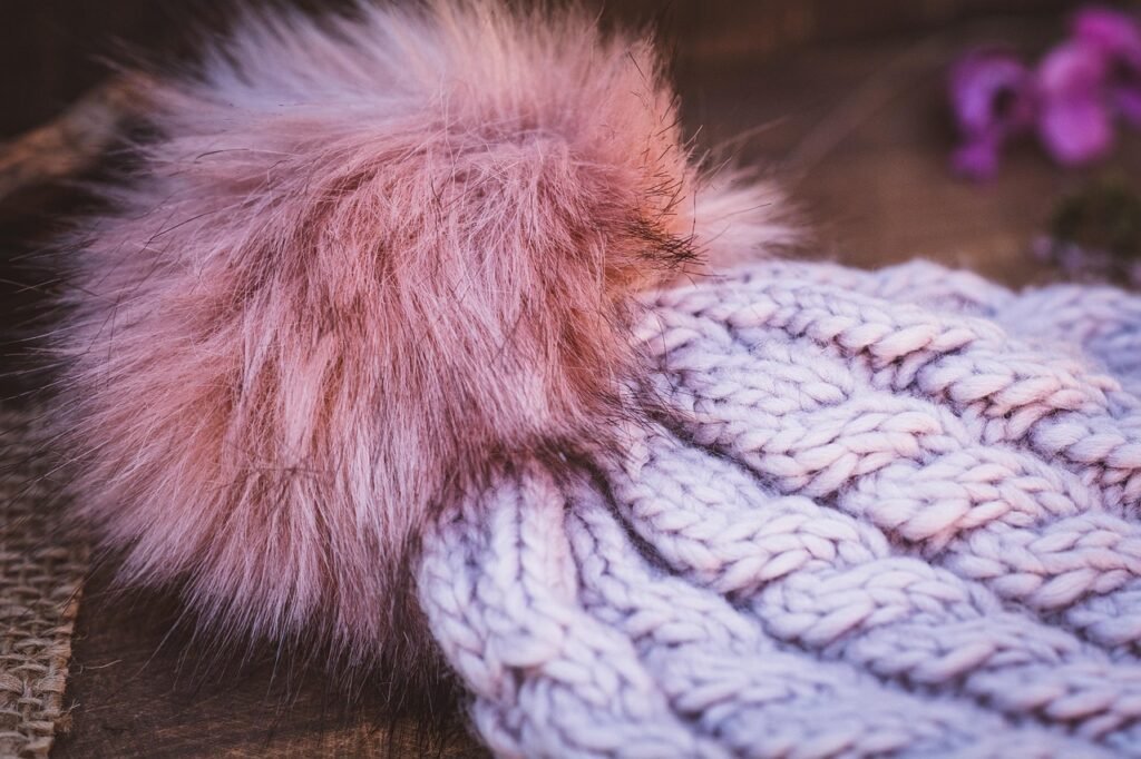 Lavender cable knit beanie topped with a fluffy pink faux fur pom pom