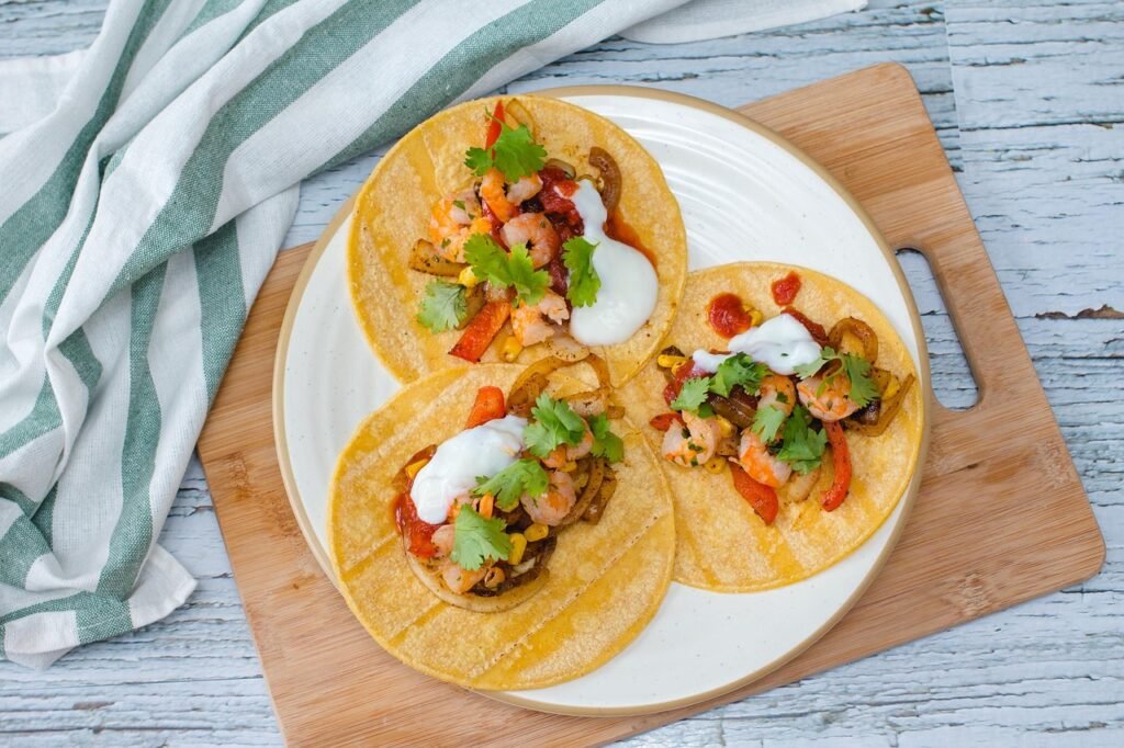 Three corn tortilla tacos topped with shrimp, cilantro and a white cream sauce on a plate
