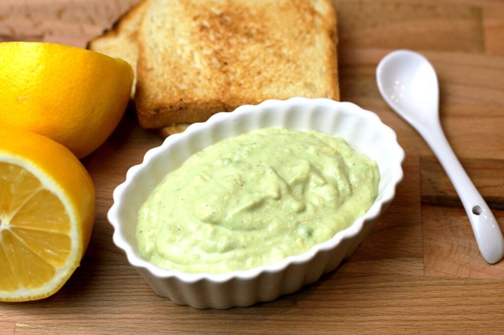 Smooth pale green cream sauce in a white dish beside lemon halves and toasted bread