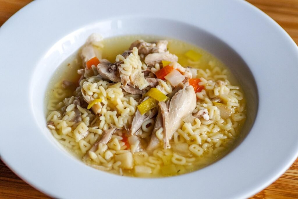 White bowl of chicken noodle soup with shredded chicken and carrots in golden broth