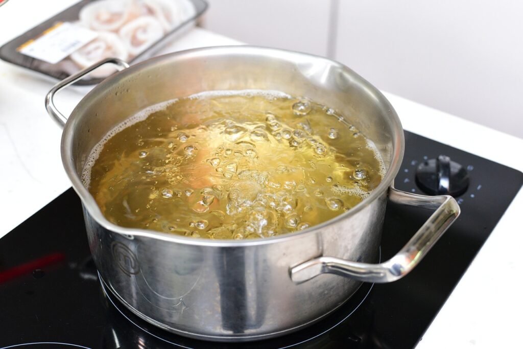 Stainless steel pot of golden broth with vegetables simmering on a black induction cooktop