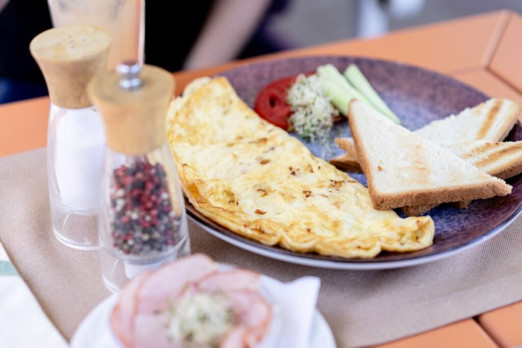 Pale folded omelette on a dark plate with toast, greens and pepper grinders
