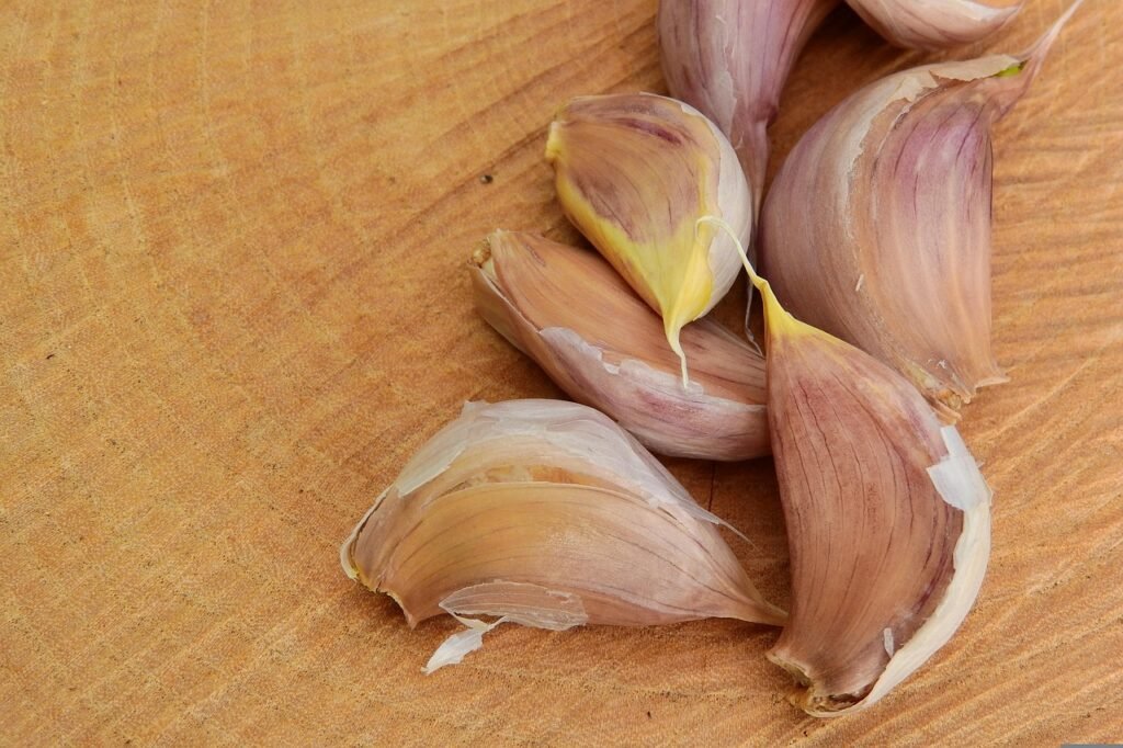 Loose unpeeled garlic cloves scattered on a light wooden cutting board