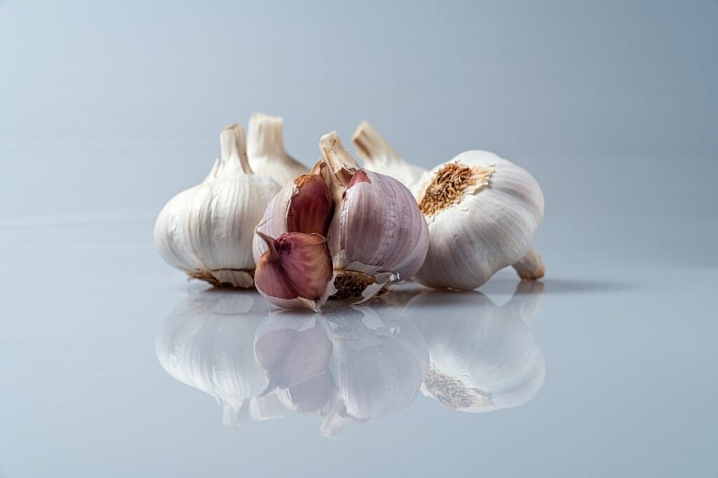 Several whole garlic bulbs and loose cloves reflected on a pale blue surface