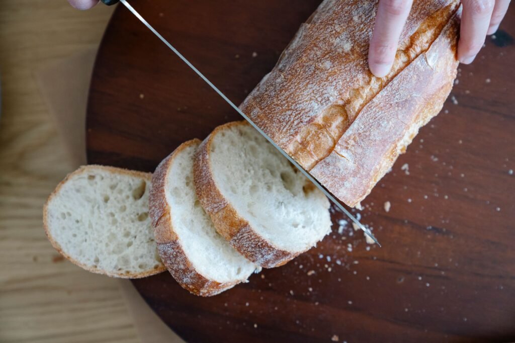 Hand slicing a crusty loaf of bread with a serrated knife on a dark wooden board