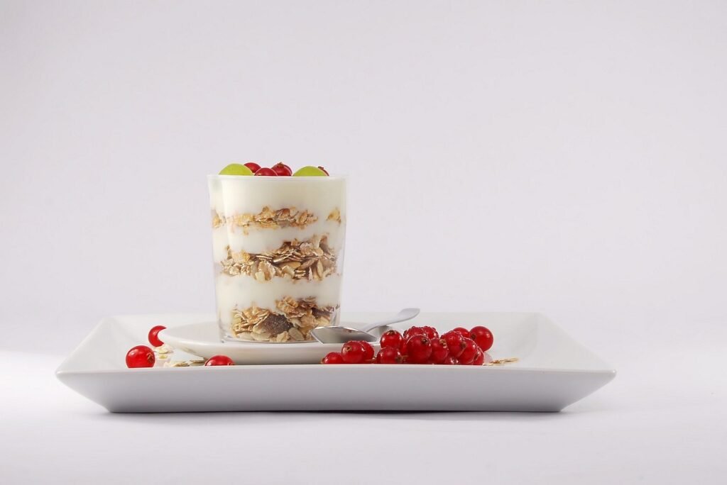 Glass layered with yogurt and granola on a white tray with red currants