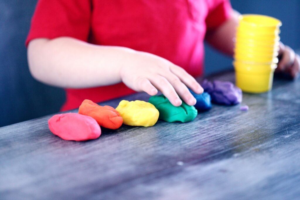 Child's hands pressing a row of colorful playdough balls on a gray wooden table