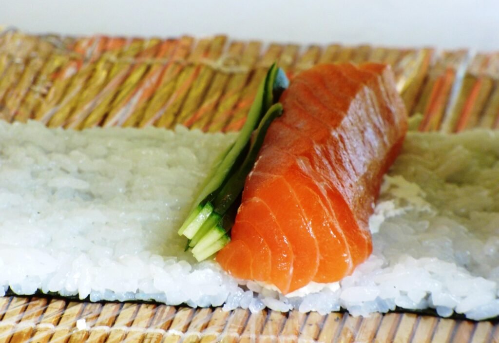 Salmon and cucumber laid over seasoned rice on a bamboo mat before rolling