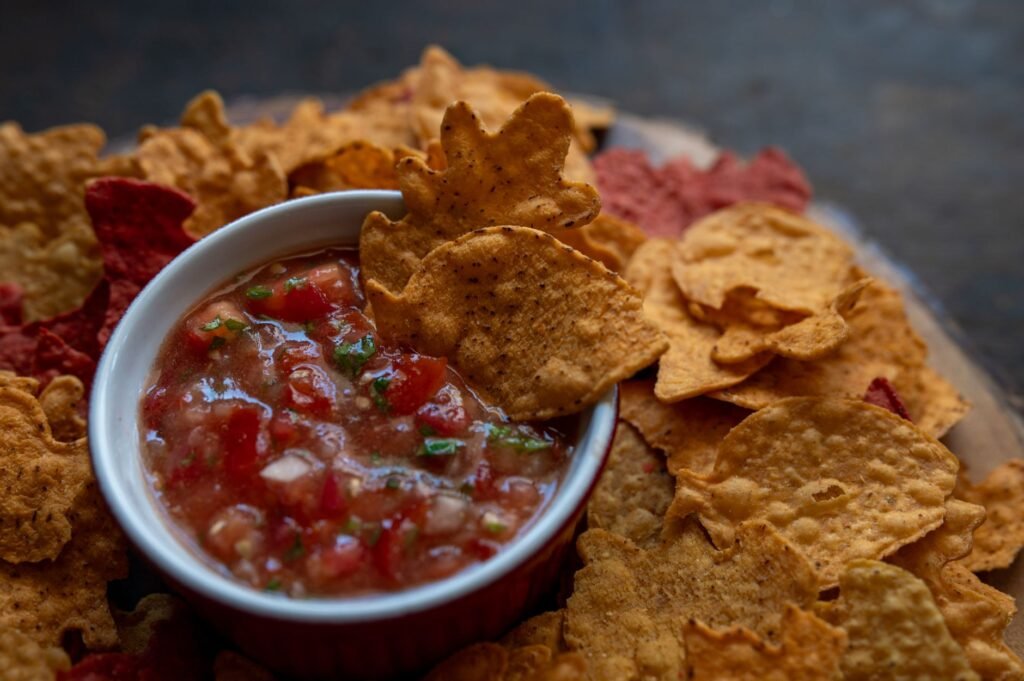 Corn tortilla chips surrounding a bowl of chunky red salsa