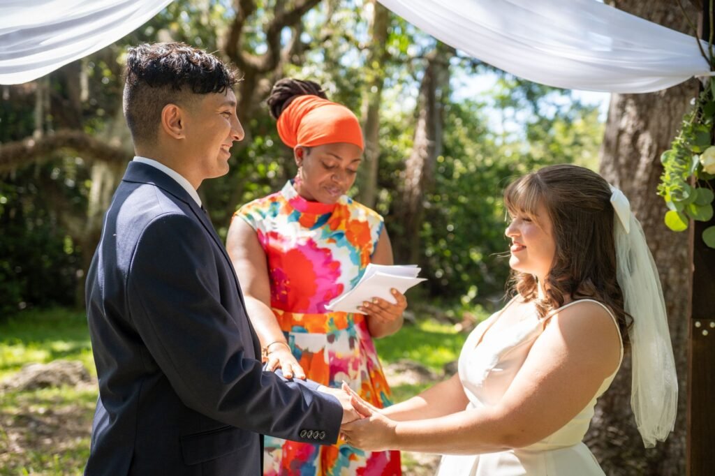 Officiant in a colorful dress reading from a card as a couple holds hands outdoors