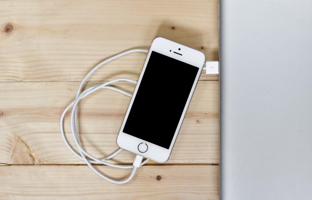 White smartphone connected to a white charging cable on a light wooden surface