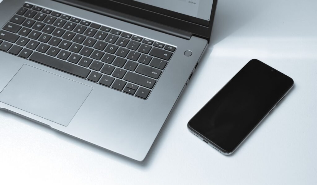 Black smartphone lying beside an open silver laptop on a white desk