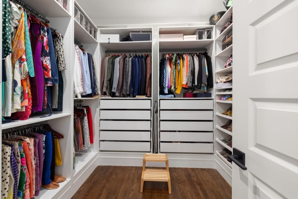 Tidy walk in closet with hanging clothes, white drawers, shoe shelves and a small wooden step stool