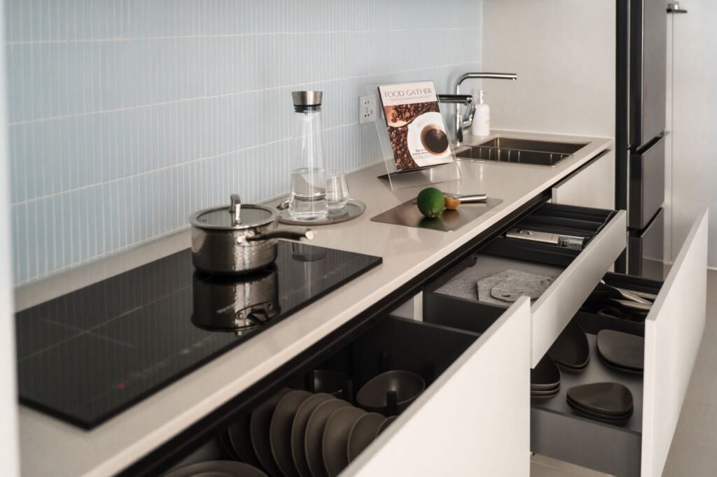 Open deep kitchen drawers holding stacked dark plates and bowls below a cooktop