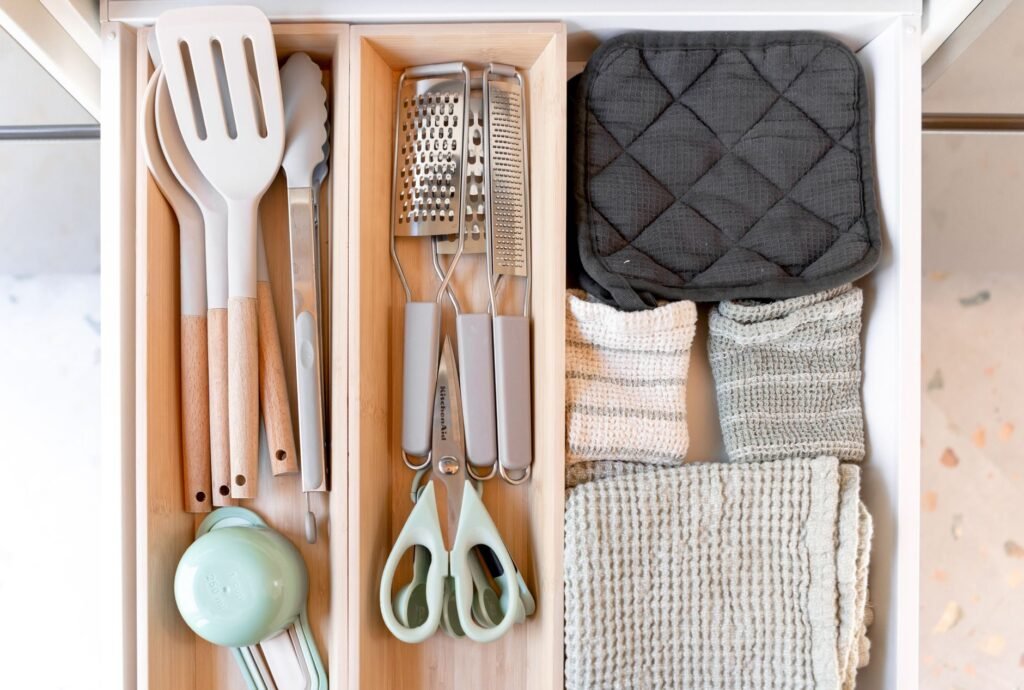 Kitchen drawer with a wooden organizer holding utensils, graters, scissors and folded towels