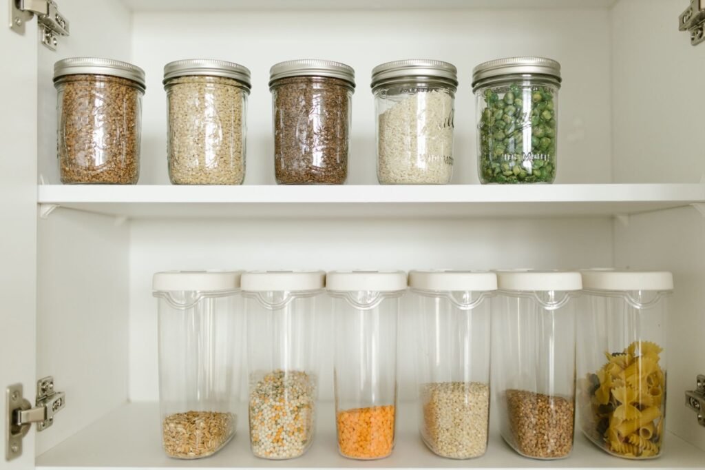 White cabinet shelves lined with clear jars of grains, beans, pasta and dried peas