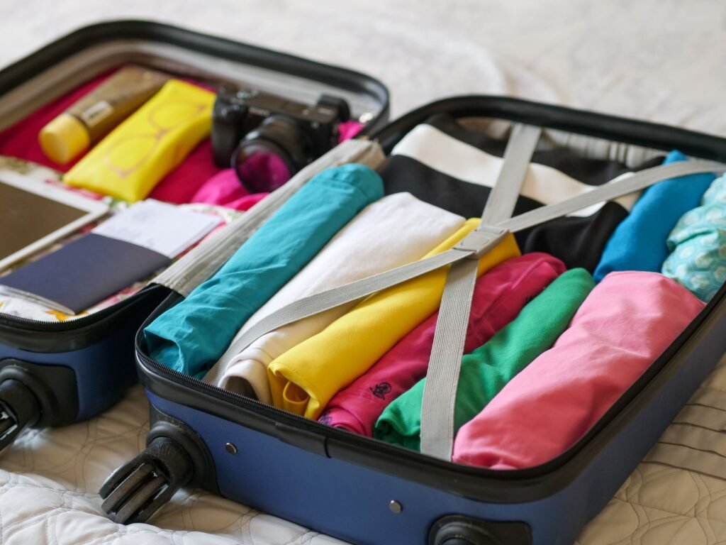 Open suitcase packed with rolled colorful clothes held down by gray straps