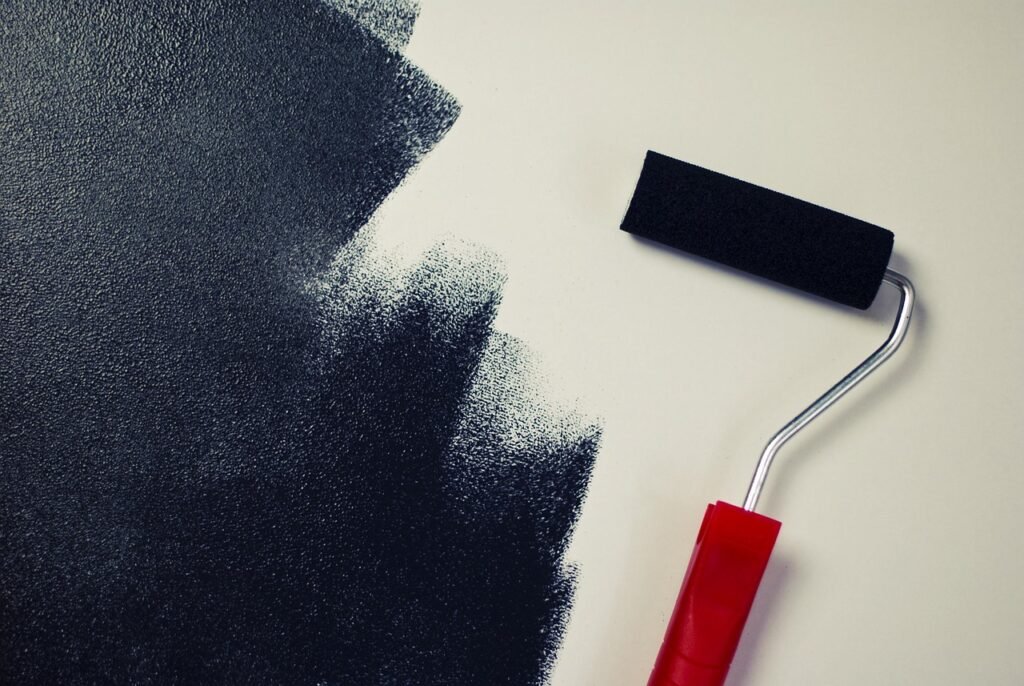 Paint roller with a red handle beside a fresh coat of dark gray paint on a pale wall