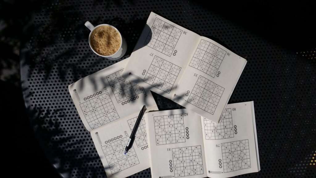 Printed sudoku puzzle sheets with a pen and a cup of coffee on dark fabric
