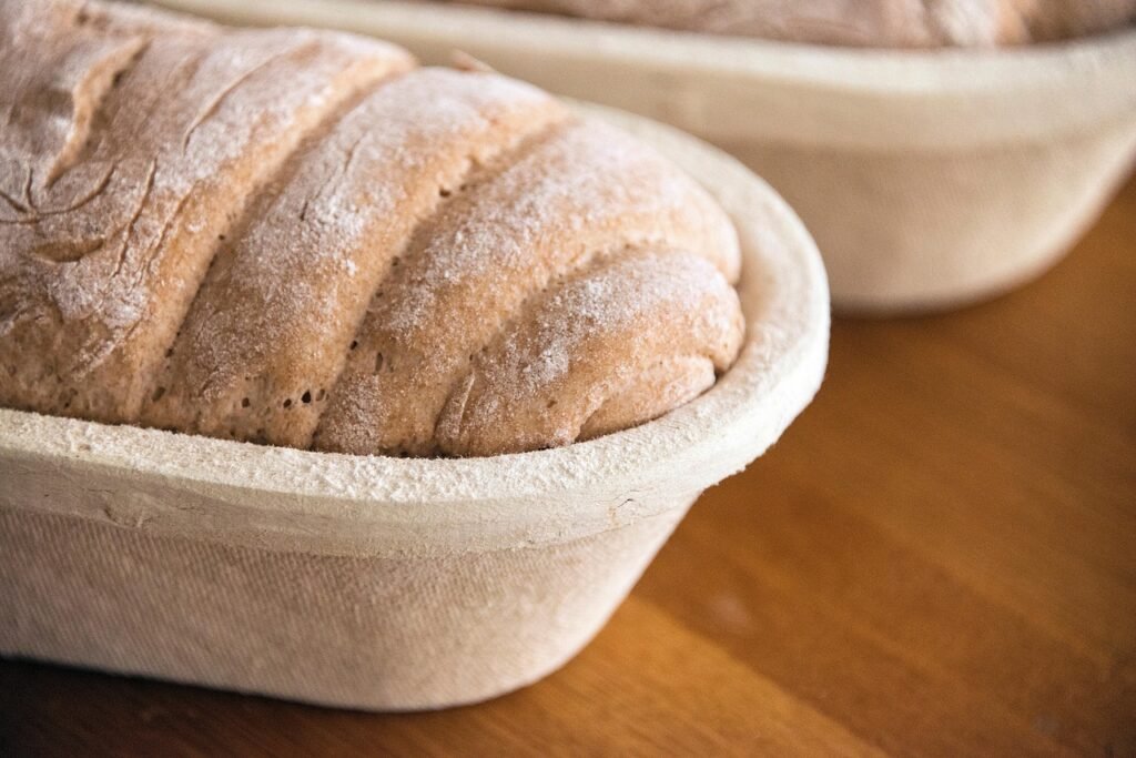 Floured loaf resting in an oval proofing basket on a wooden counter