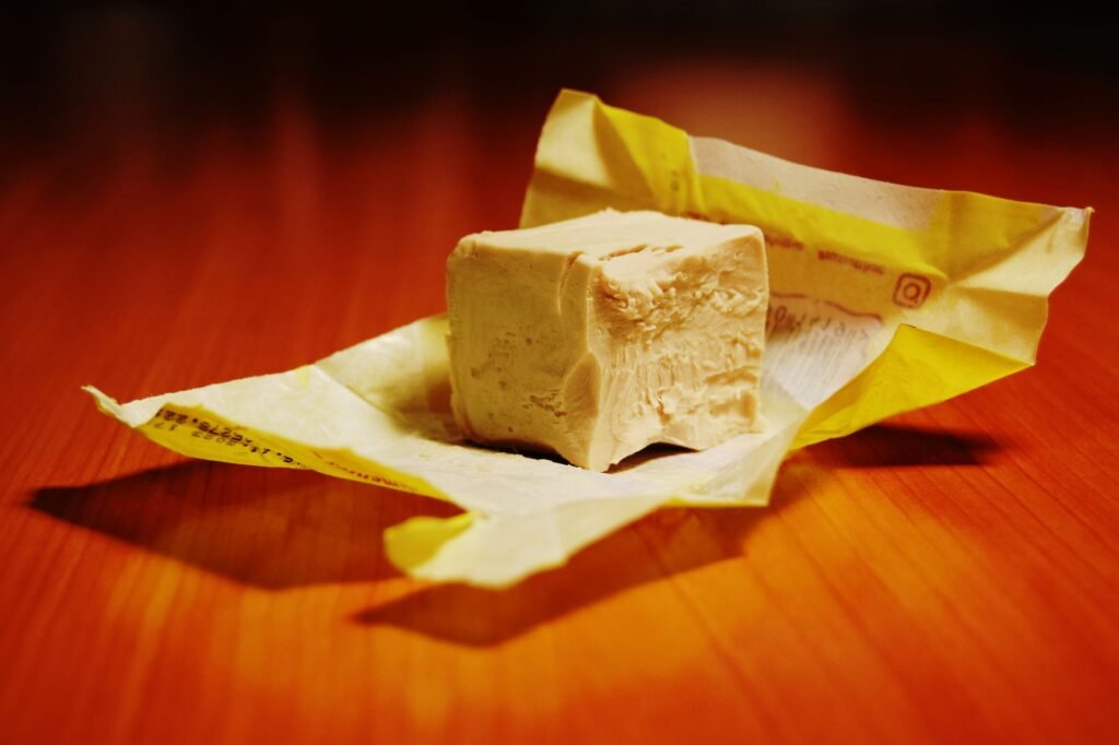 Block of fresh compressed yeast on an unfolded yellow wrapper on a warm orange surface