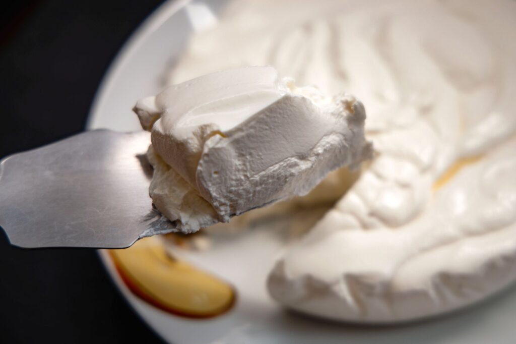 A palette knife lifting a piece of soft cream cheese from a white plate
