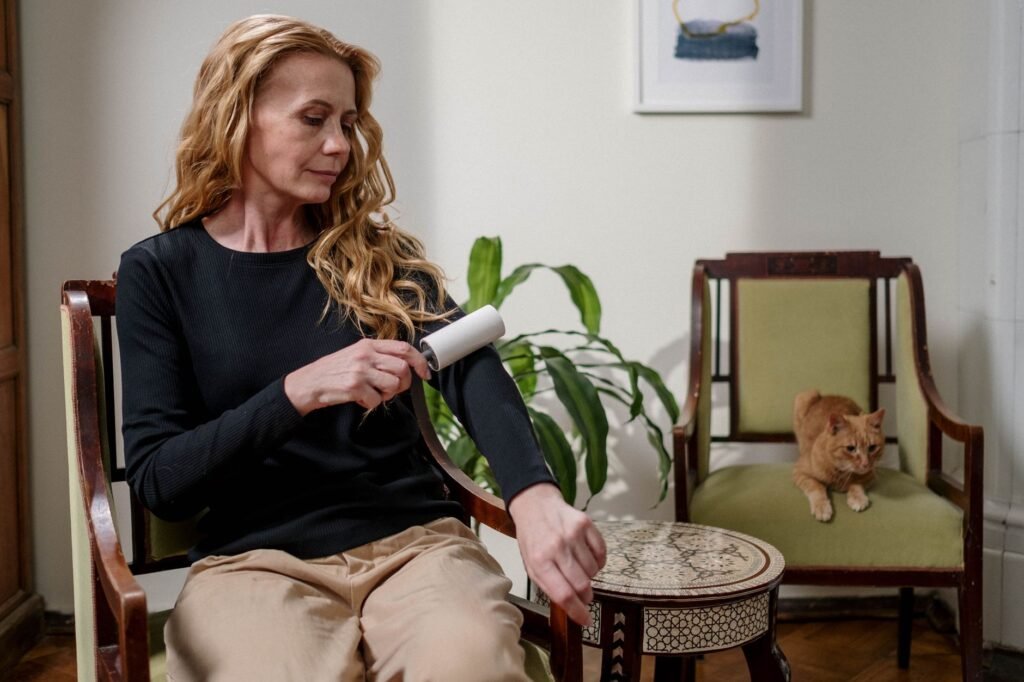 Woman in a black sweater using a lint roller on her sleeve while a cat sits nearby