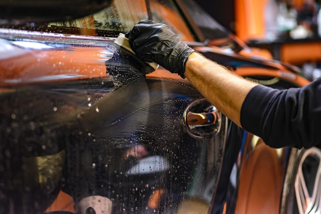 Gloved hand wiping wet orange car paint with a cloth